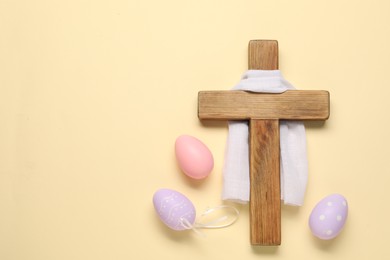 Wooden cross, white cloth and painted Easter eggs on beige background, flat lay. Space for text