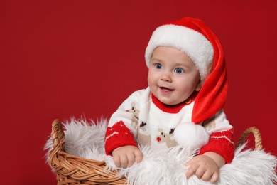 Cute baby in wicker basket on red background, space for text. Christmas celebration
