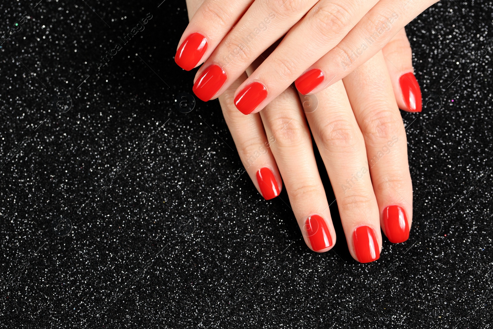 Photo of Woman showing manicured hands with red nail polish on black background, top view. Space for text