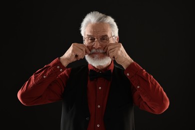 Senior man touching mustache on black background