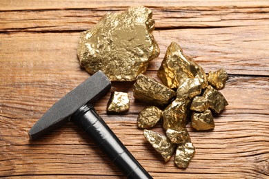Photo of Pile of gold nuggets and hammer on wooden table, flat lay
