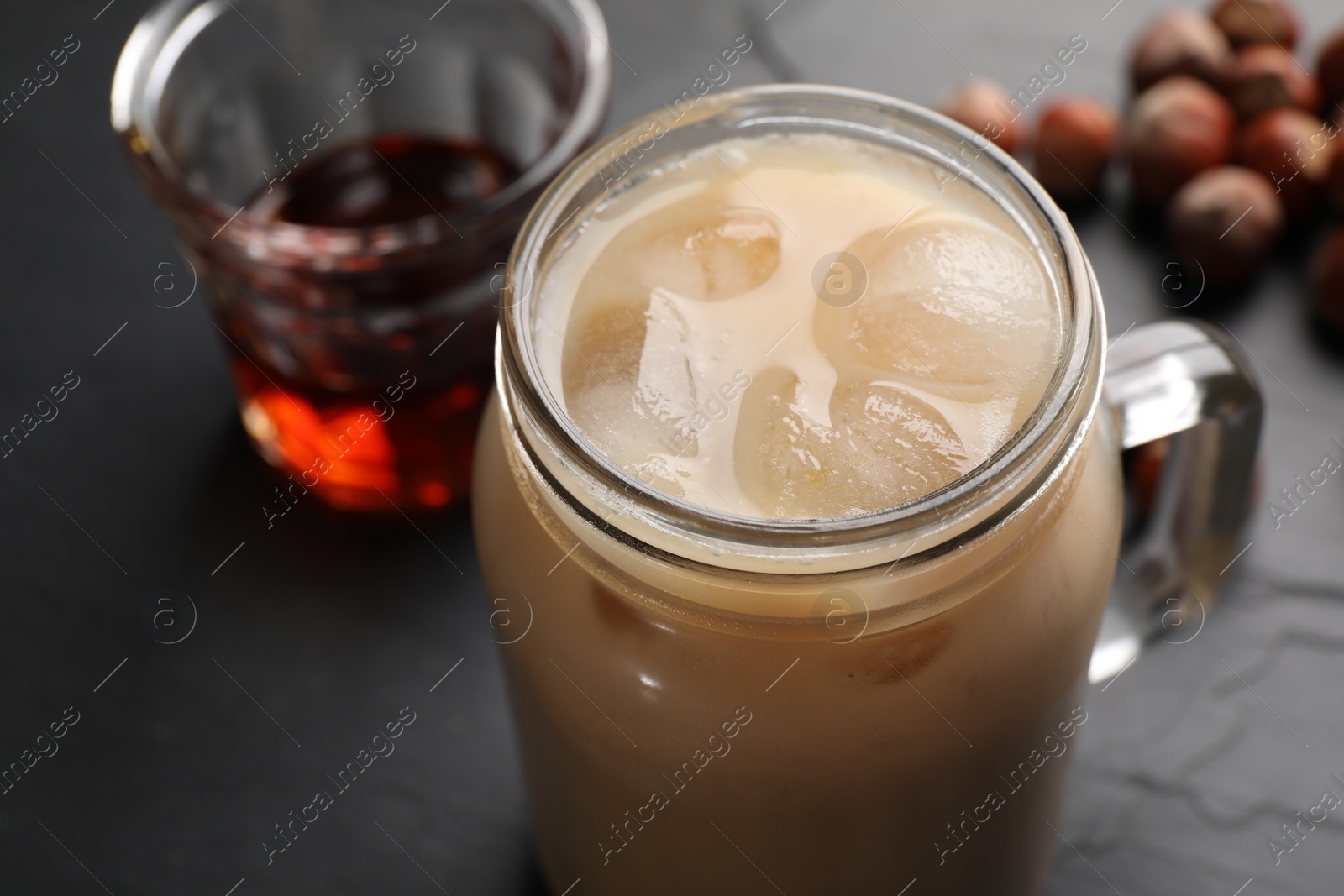 Photo of Mason jar of delicious iced coffee, syrup and hazelnuts on black table, closeup