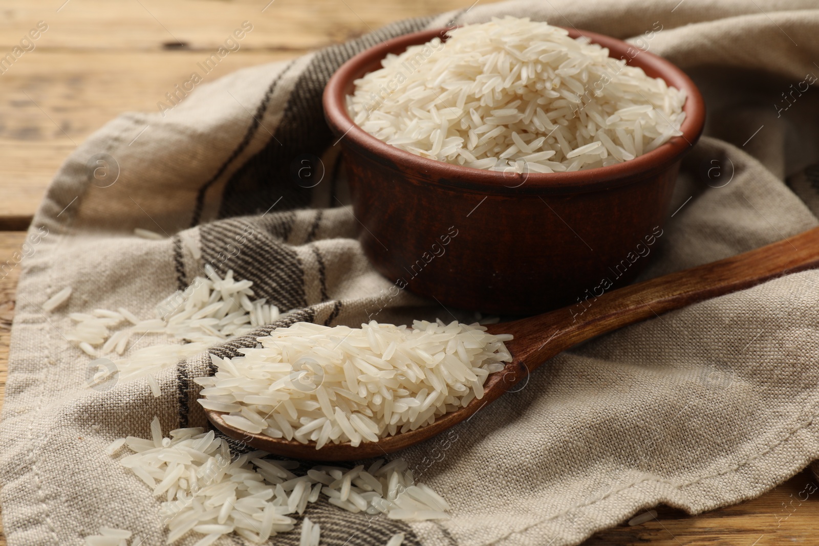 Photo of Raw basmati rice in bowl and spoon on table, closeup