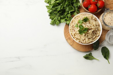 Photo of Tasty quinoa porridge with parsley in bowl on white marble table, flat lay. Space for text