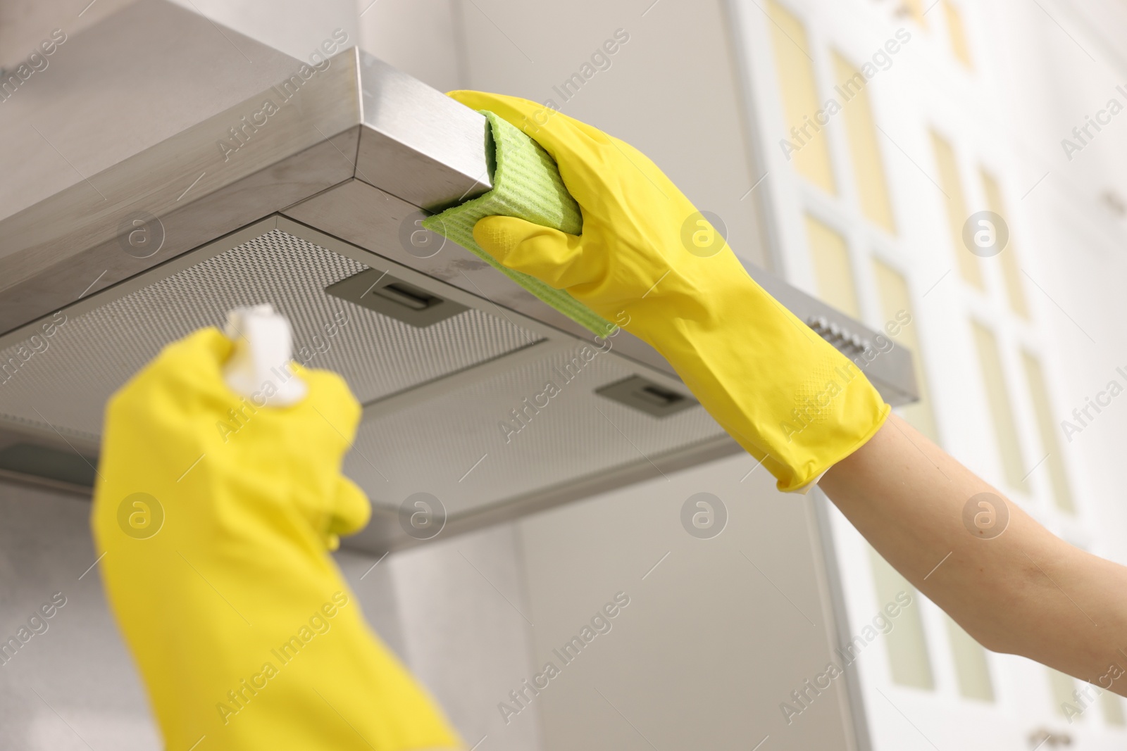 Photo of Woman with spray bottle and microfiber cloth cleaning kitchen hood indoors, closeup