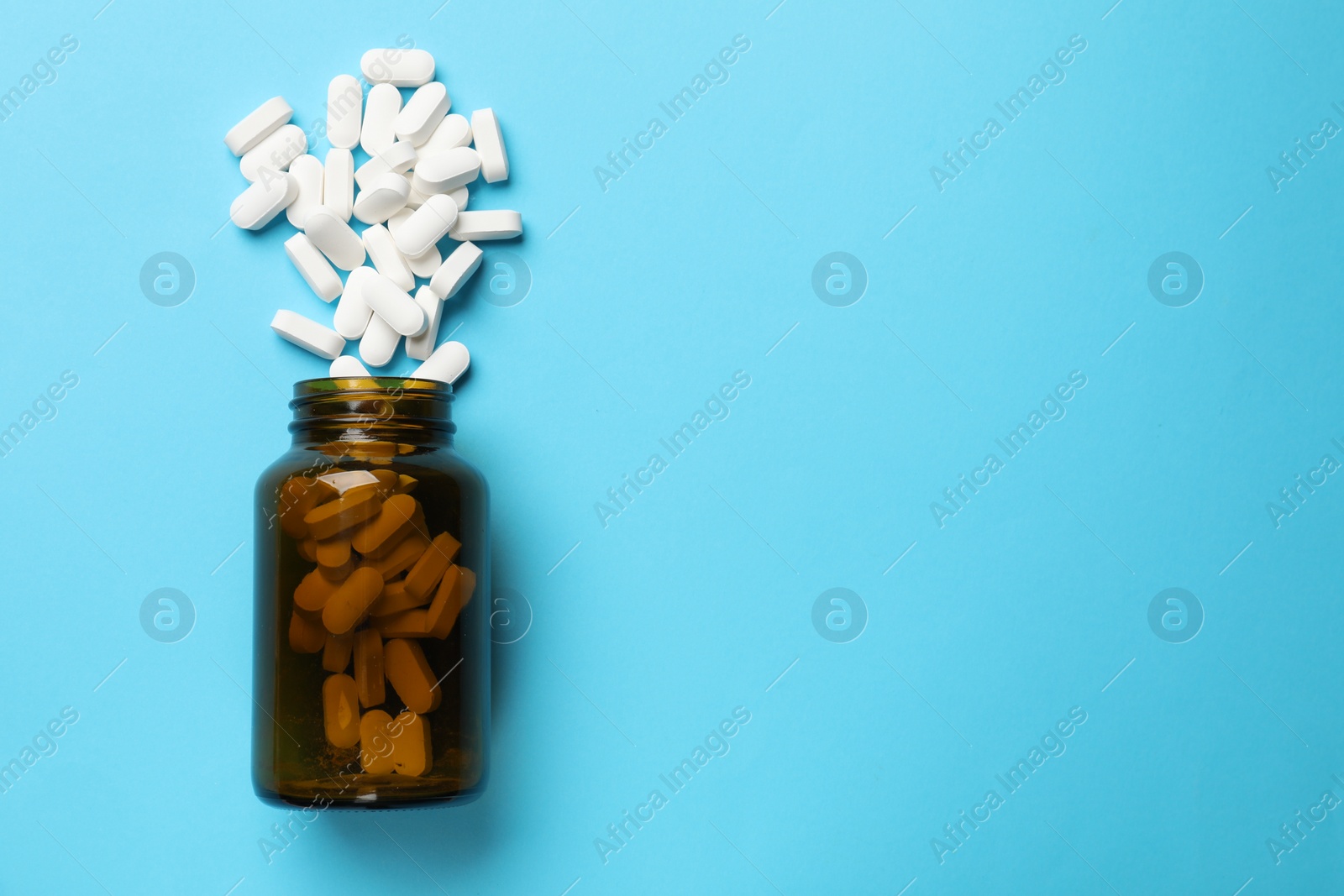 Photo of Bottle and vitamin capsules on light blue background, top view. Space for text