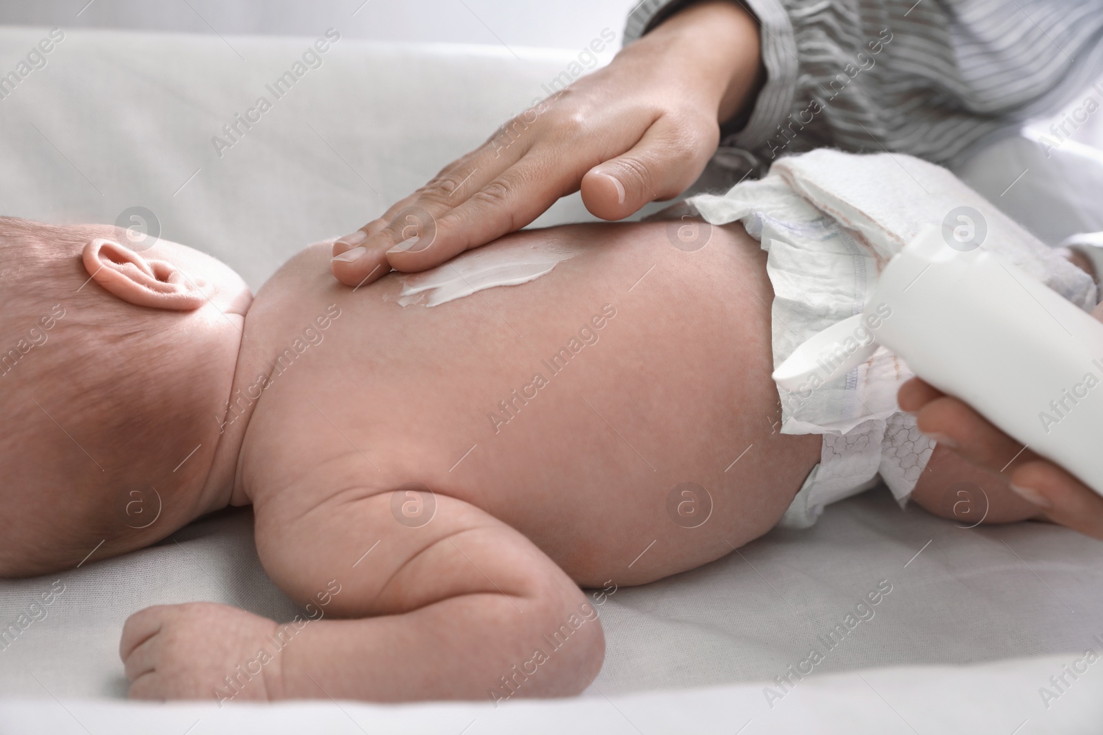 Photo of Mother applying moisturizing cream onto baby`s back on changing table, closeup