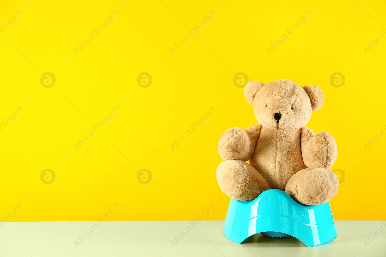 Photo of Teddy bear with blue potty on table against yellow background, space for text. Toilet training
