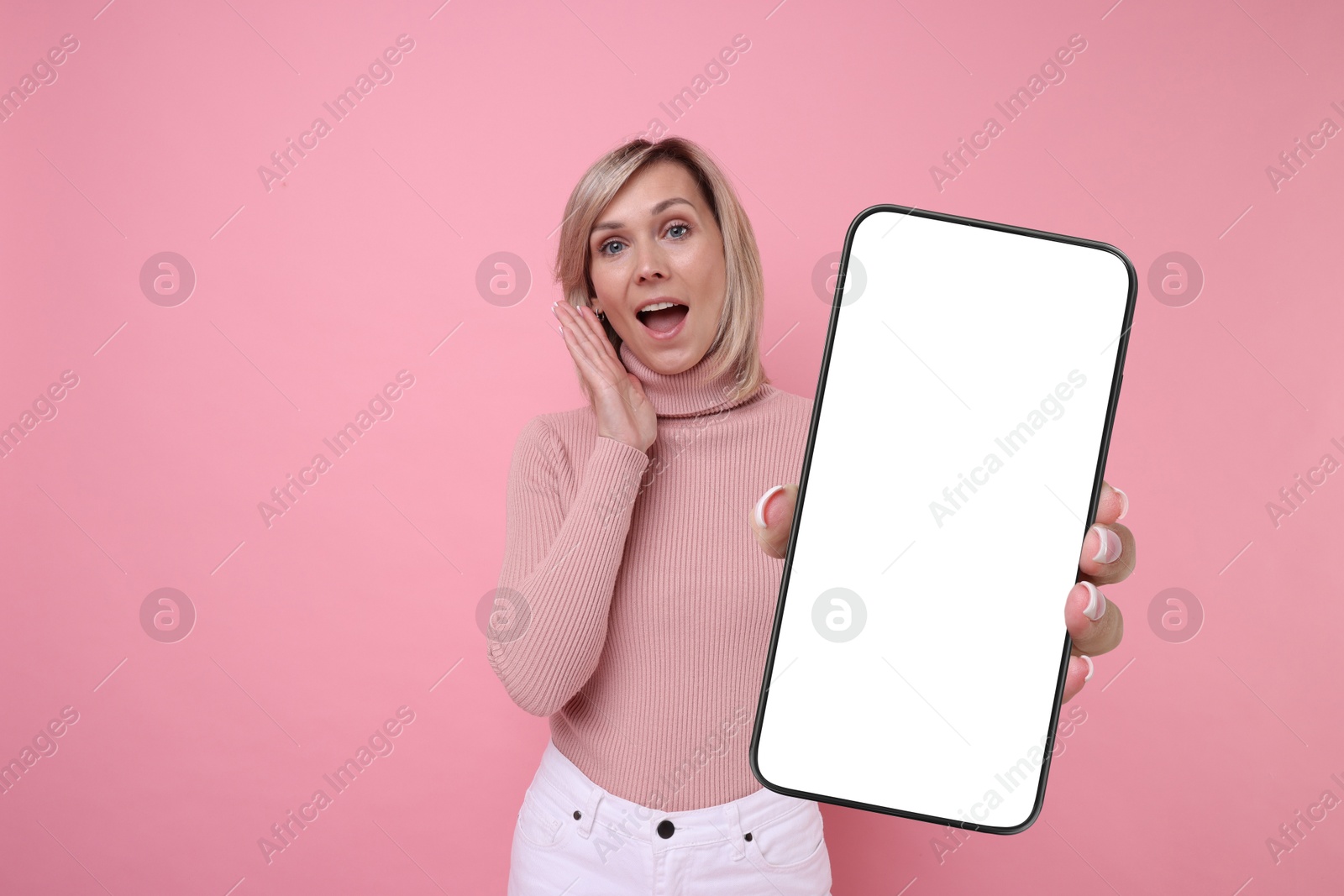 Image of Woman showing mobile phone with blank screen on pink background. Mockup for design