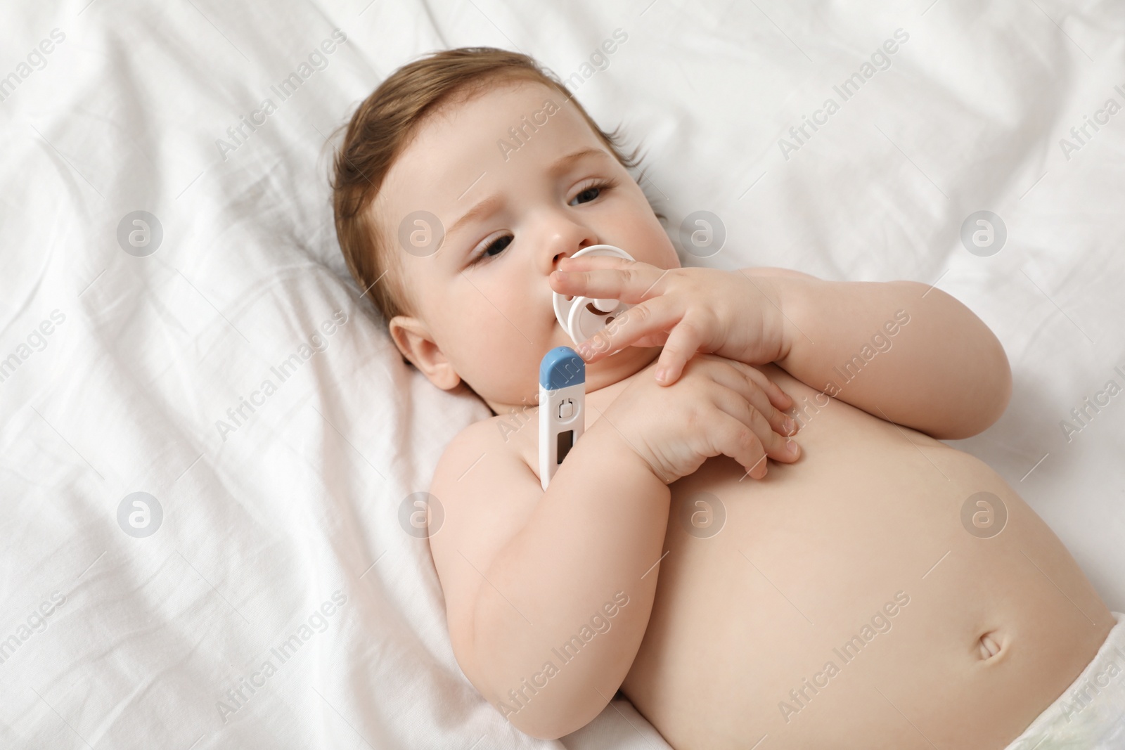 Photo of Adorable baby with thermometer on bed. Measuring temperature