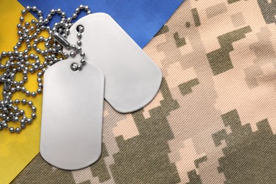 Photo of Military ID tags and Ukrainian flag on pixel camouflage, flat lay. Space for text