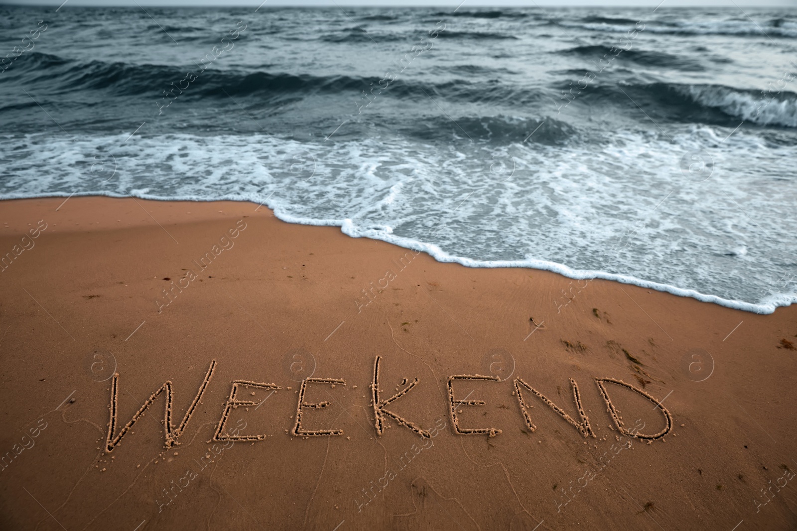 Photo of Sea wave rolling onto sandy beach with written word Weekend