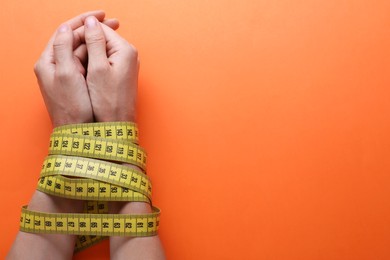 Photo of Woman tied with measuring tape on orange background, top view and space for text. Diet concept