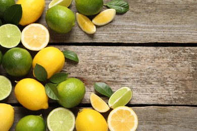 Fresh ripe lemons, limes and green leaves on wooden background, flat lay. Space for text