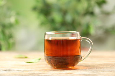 Cup of black tea on wooden table against blurred background