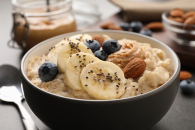 Photo of Tasty oatmeal porridge with toppings served in bowl on table, closeup