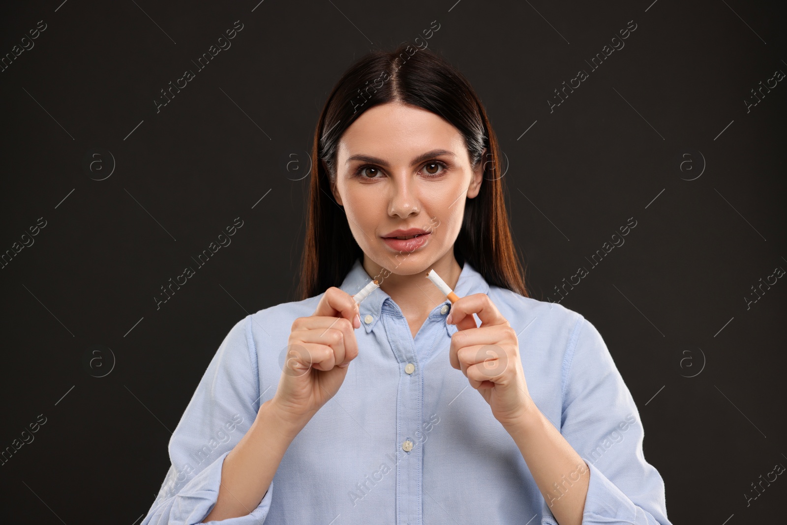 Photo of Stop smoking concept. Woman breaking cigarette on black background