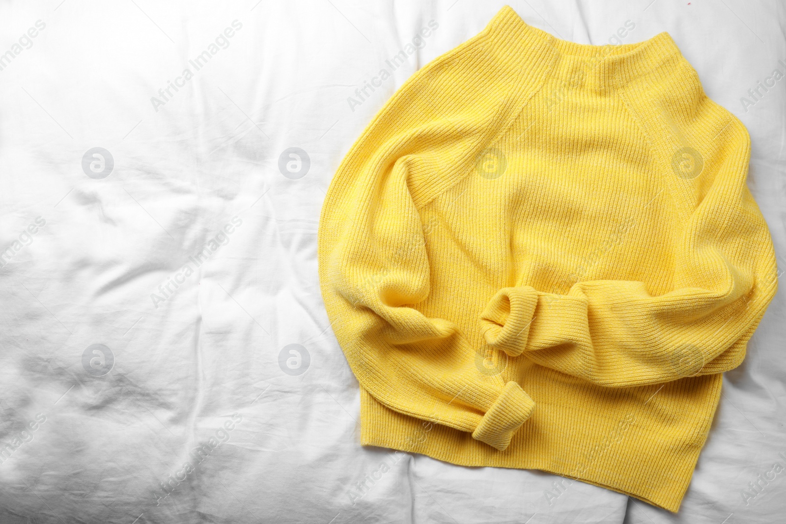 Photo of Yellow warm sweater on white bedsheet, top view. Space for text