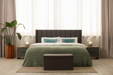 Photo of Comfortable bed, bedside tables and ottoman in bedroom