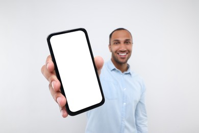 Photo of Young man showing smartphone in hand on white background, selective focus. Mockup for design