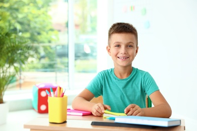 Photo of Little boy with school stationery at desk in classroom