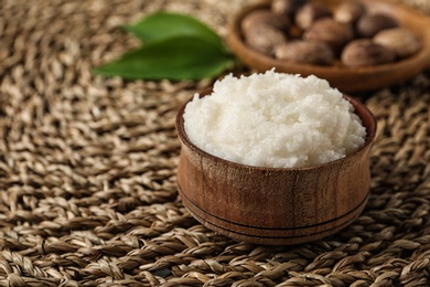 Photo of Shea butter in bowl and nuts on wicker mat, closeup. Space for text