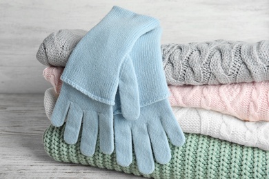 Photo of Stacked sweaters and gloves on wooden table, closeup. Autumn clothes