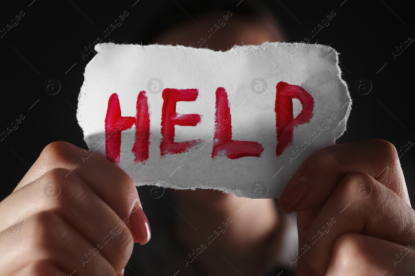 Photo of Woman holding piece of paper with word Help on black background, closeup. Domestic violence concept