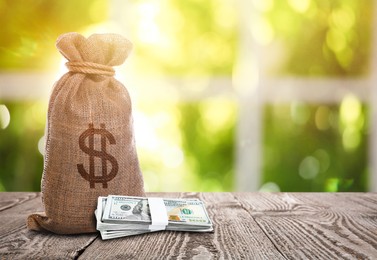 Image of Burlap bag with dollar sign and banknotes on wooden table indoors. Space for text