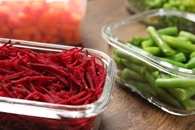 Containers with cut beetroot and green beans on wooden table, closeup. Food storage