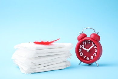 Photo of Packed menstrual pads with red feather and alarm clock on color background. Gynecological care