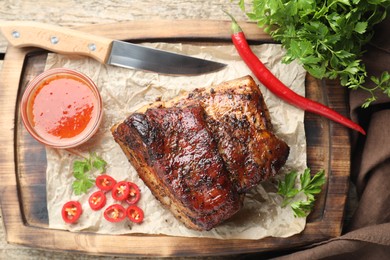 Photo of Piece of baked pork belly served with sauce and chili pepper on wooden table, top view