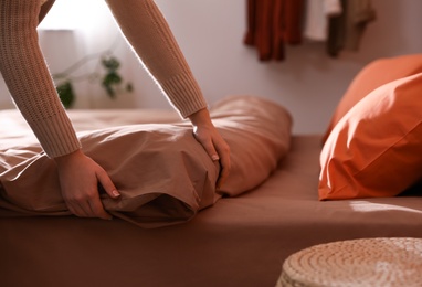 Photo of Woman making bed with fresh linens and orange pillow, closeup