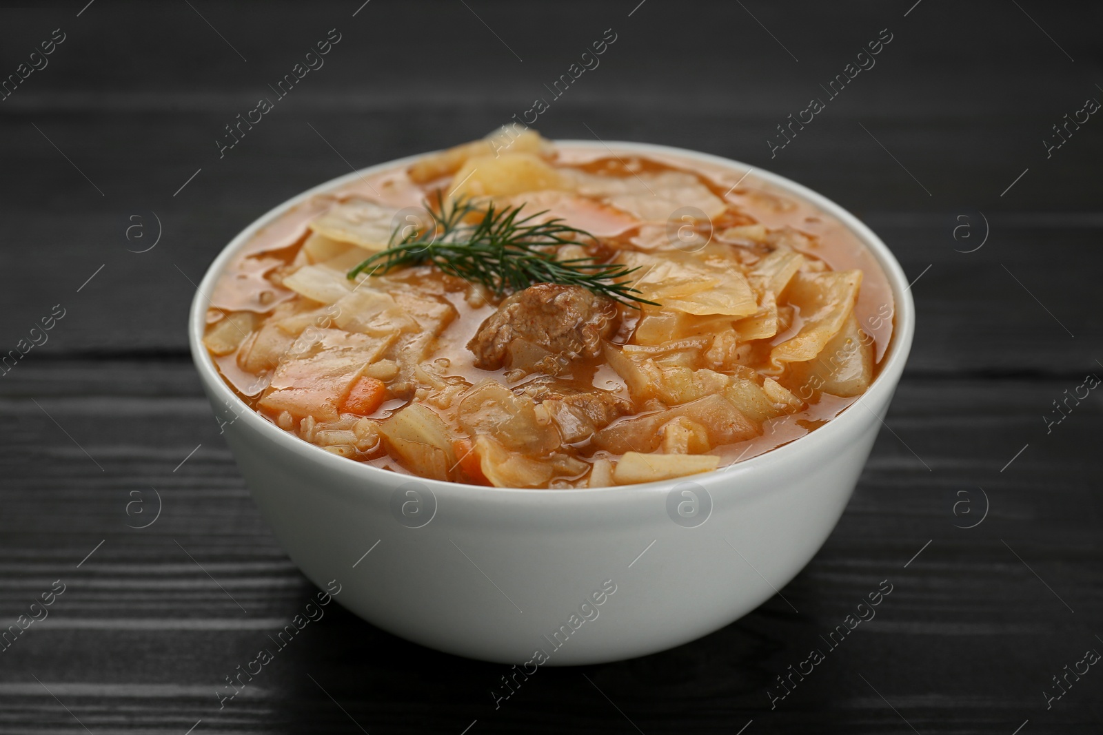 Photo of Tasty cabbage soup with meat, carrot and dill on black wooden table, closeup