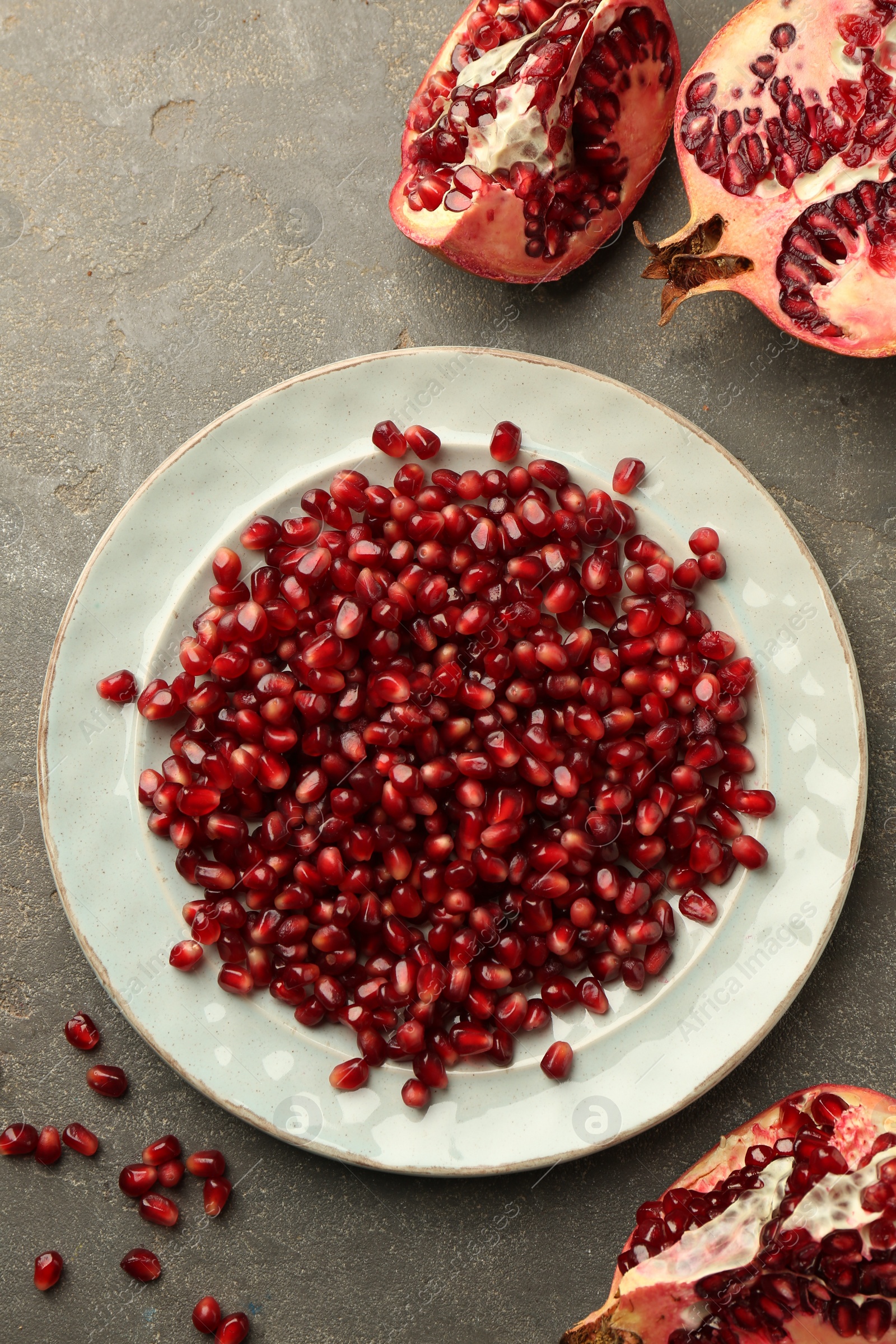 Photo of Tasty ripe pomegranate and grains on grey table, flat lay