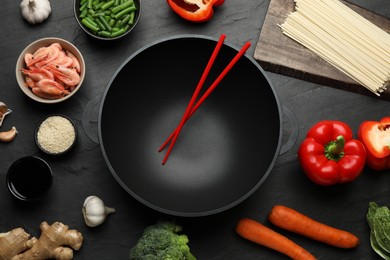 Photo of Empty iron wok with chopsticks and raw ingredients on black table, flat lay