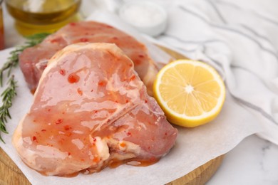 Board with raw marinated meat, lemon and rosemary on white table, closeup