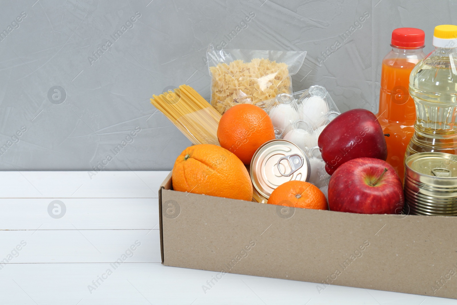 Photo of Humanitarian aid. Different food products for donation in box on white wooden table. Space for text