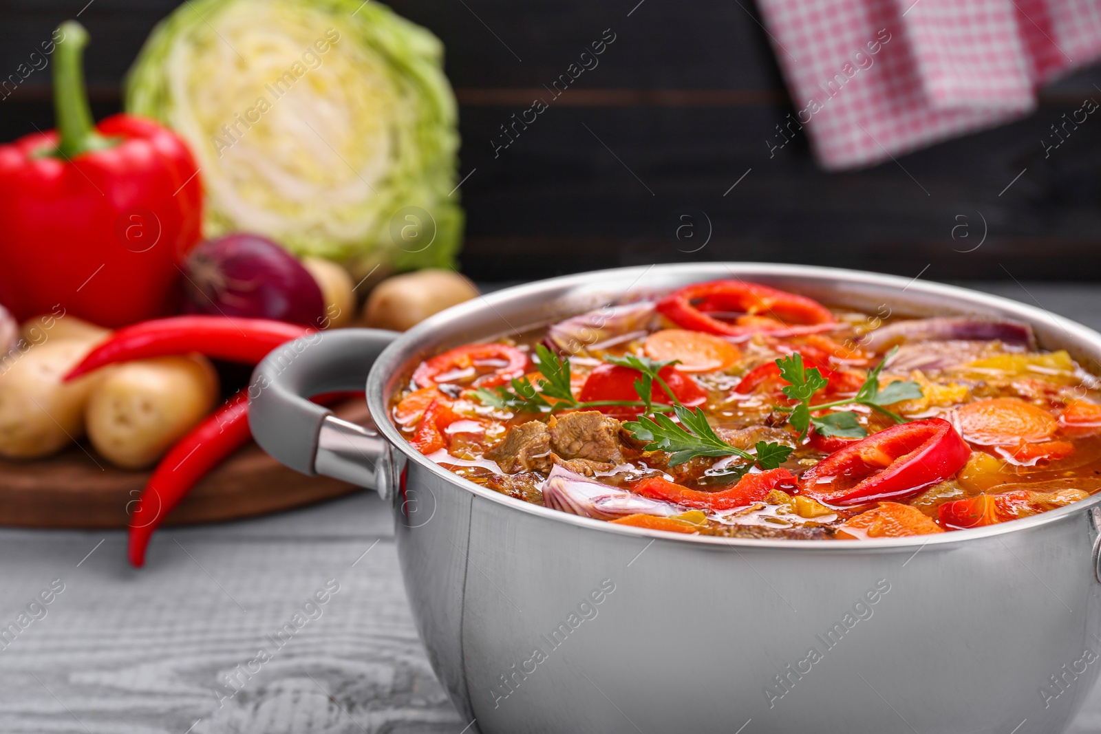 Photo of Saucepan of delicious vegetable soup with meat and ingredients on grey wooden table, closeup. Space for text