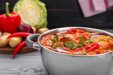 Photo of Saucepan of delicious vegetable soup with meat and ingredients on grey wooden table, closeup. Space for text