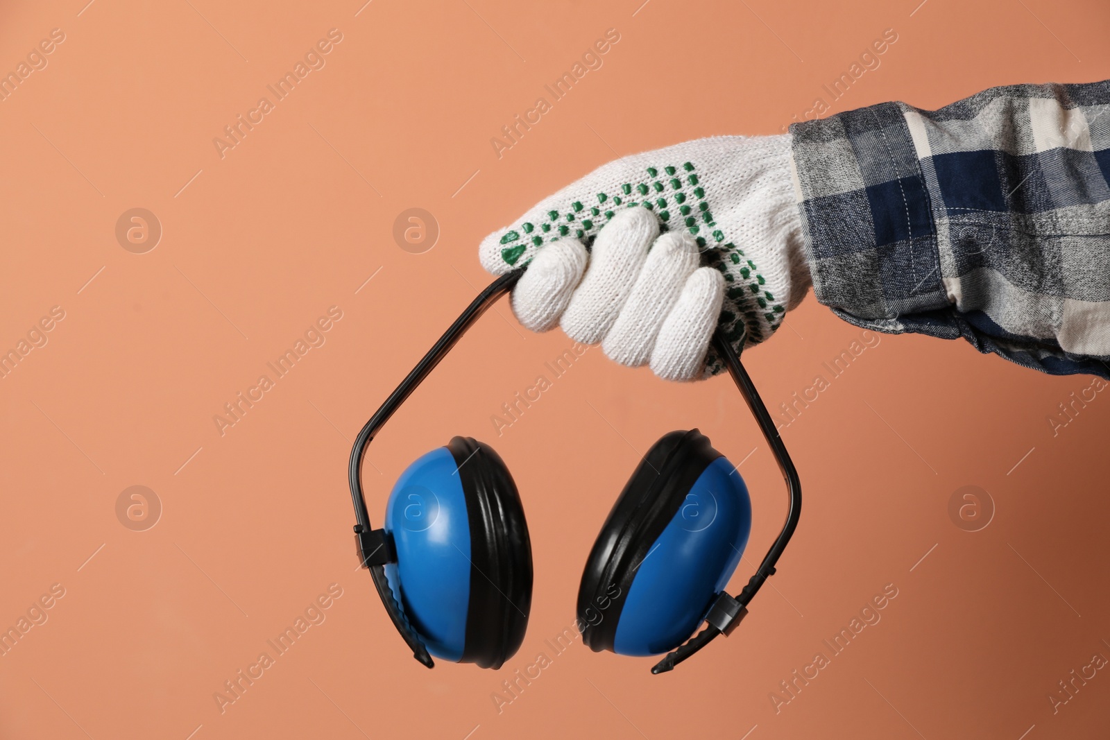 Photo of Worker holding safety headphones on coral background, closeup. Hearing protection device