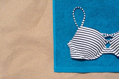 Blue beach towel and swimsuit on sand, top view. Space for text