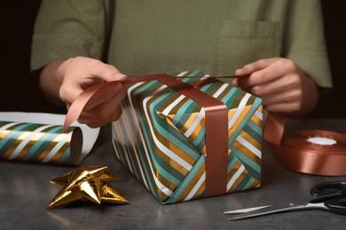 Photo of Woman wrapping gift at grey table, closeup