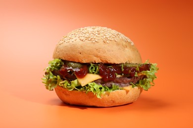 Photo of Delicious cheeseburger with lettuce, pickle, ketchup and patty on coral background, closeup