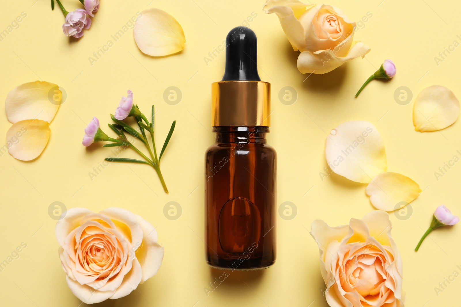 Photo of Bottle of cosmetic serum, beautiful flowers and petals on pale yellow background, flat lay