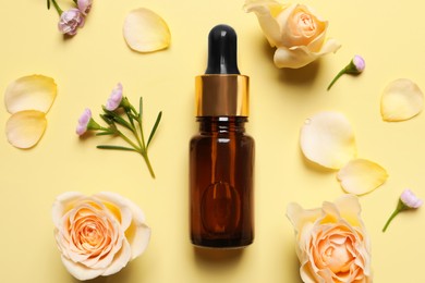 Bottle of cosmetic serum, beautiful flowers and petals on pale yellow background, flat lay