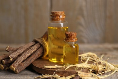 Photo of Dried sticks of licorice root and bottles of essential oil on wooden table