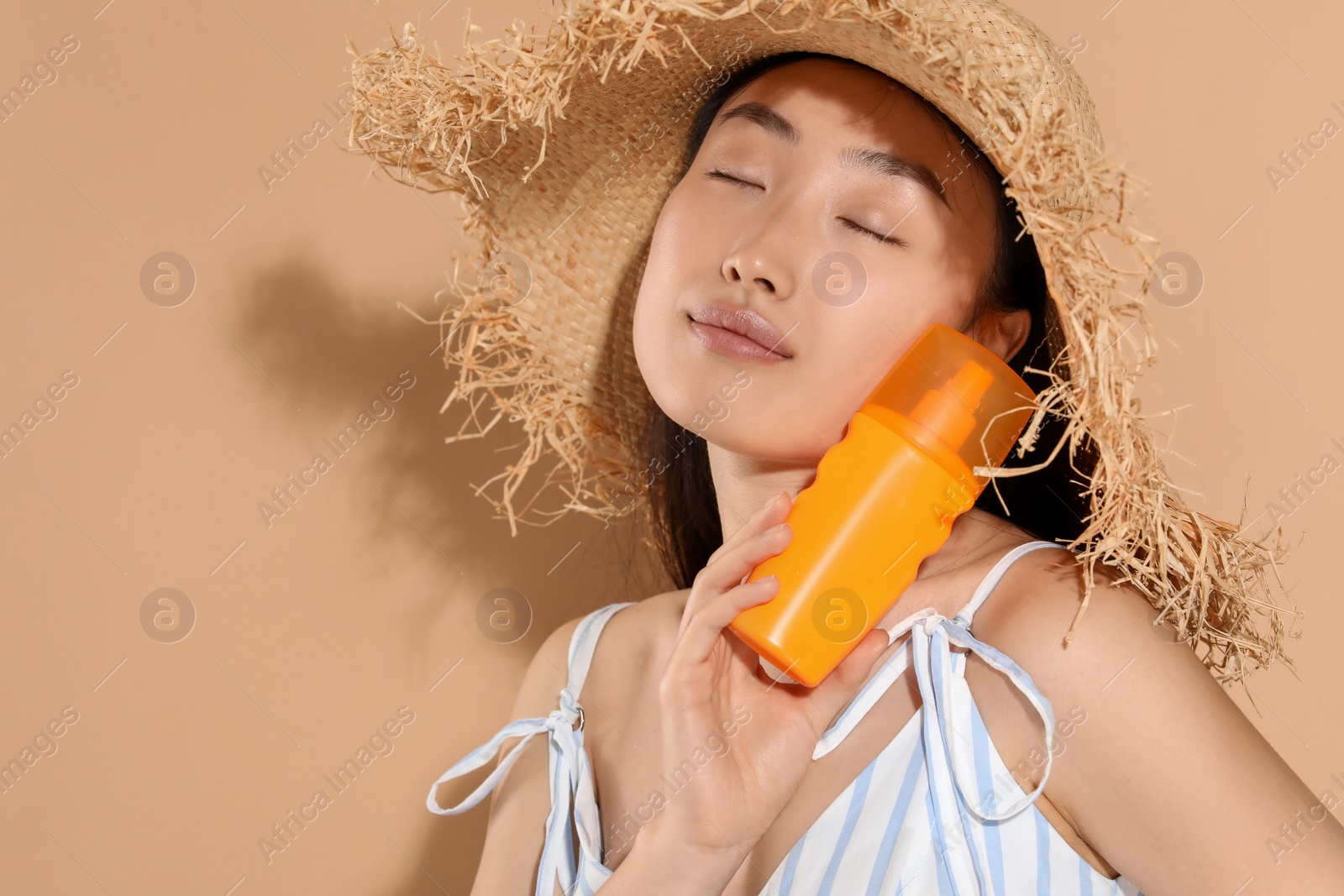 Photo of Beautiful young woman in straw hat holding sun protection cream on beige background, space for text