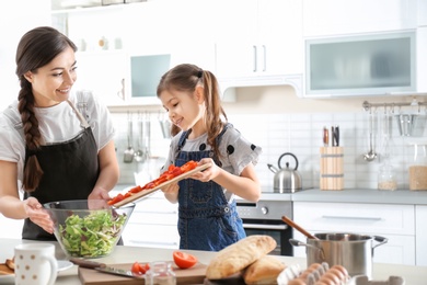 Young nanny with cute little girl cooking together in kitchen