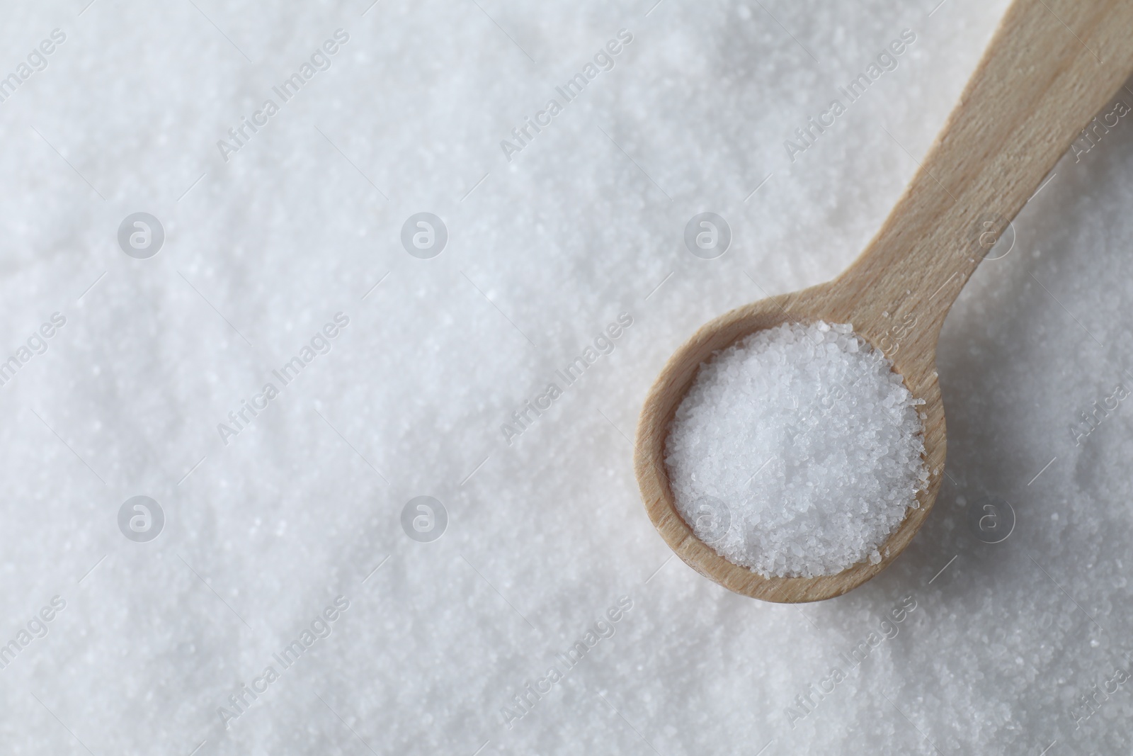 Photo of Wooden spoon on white sea salt, top view. Space for text